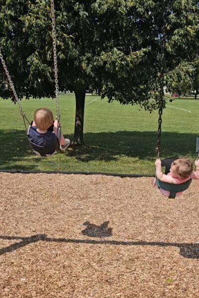 two children on swings at the park with a grassy field in the background
